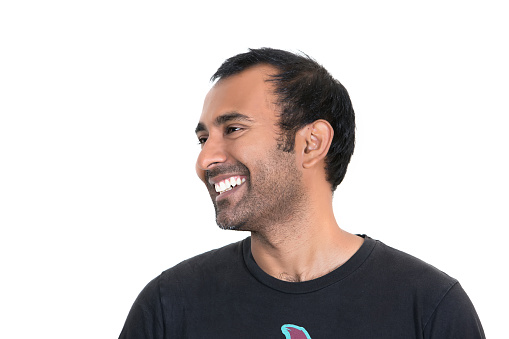 Profile of an man of Indian ethnicity with dark hair, a receding hairline and a dark five o'clock shadow on his face. Shot with a Canon 5D Mark 3 camera. He is wearing a plan black t shirt. rm