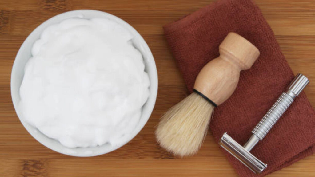 Shaving accessories on wooden background. Razor, brush, towel and foam in bowl.