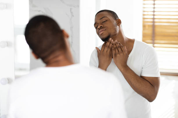 Ingrown Hair Problem. Portrait Of Unshaved Black Guy Touching Neck With Bristle While Standing Near Mirror In Bathroom, Unhappy African American Man Making Morning Beauty Routine At Home