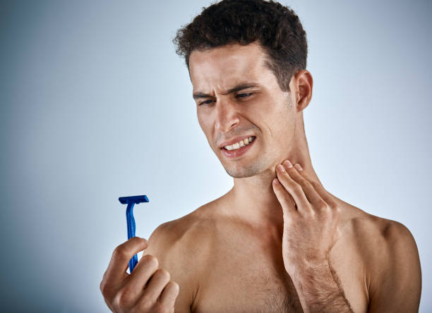 Young man grimaces as he hurts himself shaving or suffers from a skin sensitivity.