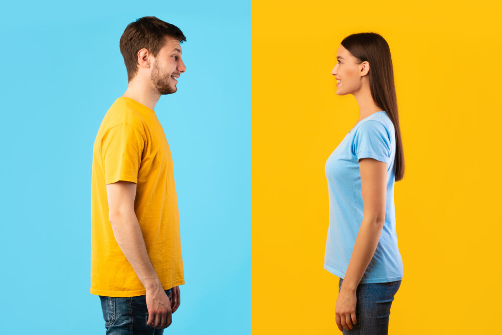 Profile portrait of casual woman and bearded smiling caucasian man posing isolated over blue and yellow studio background. Side view of positive couple standing and looking at each other