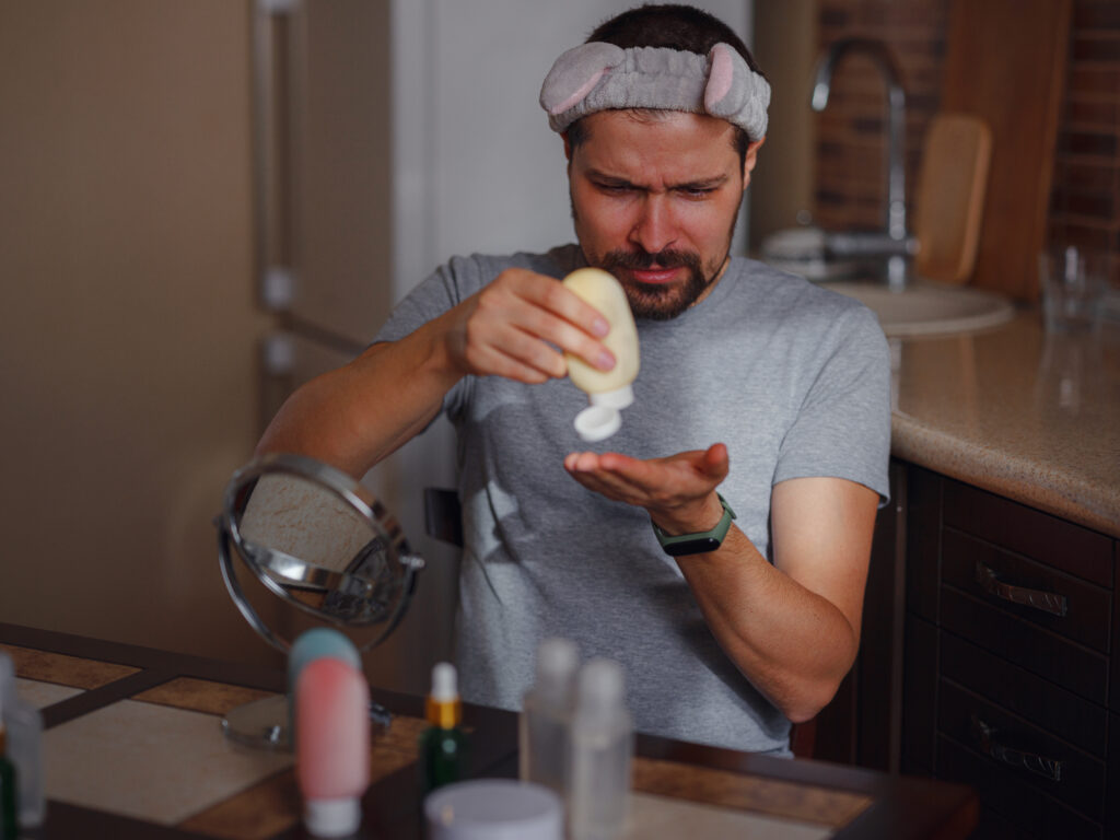 Men's beauty concept. caucAsian guy checking his skin. man with beard squeezes out skin care cream, Men's hand using moisturizing cream, skin and hand care.