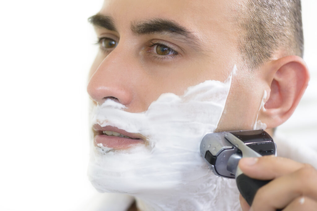 Young man shaving using electric shaver